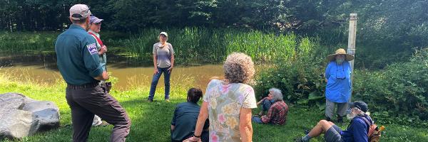 Lake Champlain Sea Grant's Marc Companion and Vermont Youth Conservation Corps' Justin Geibel (far left) conduct a stormwater training session at Frog Pond in Hubbard Park in Montpelier, Vermont in July 2020. Photo: Anna Hildebrand Group of people at a Green Infrastructure training near a wooded pond